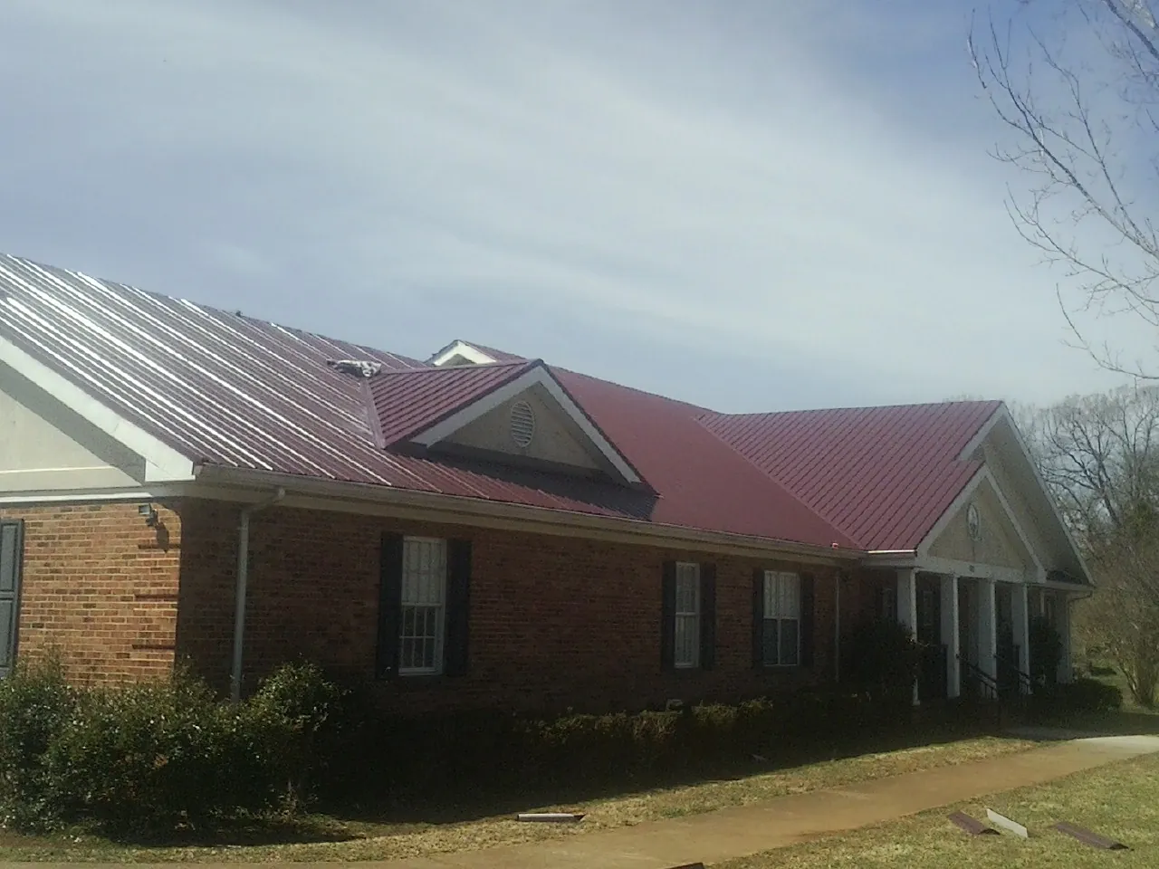 Red metal roof with gabled entries on a long brick building, from a Hail Damage Roof Repair job in New Orleans
