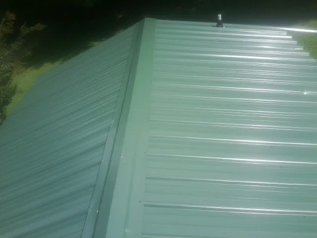 New green metal panels meeting at the ridge of a roof — Flat Roof Repair work by our crew in New Orleans