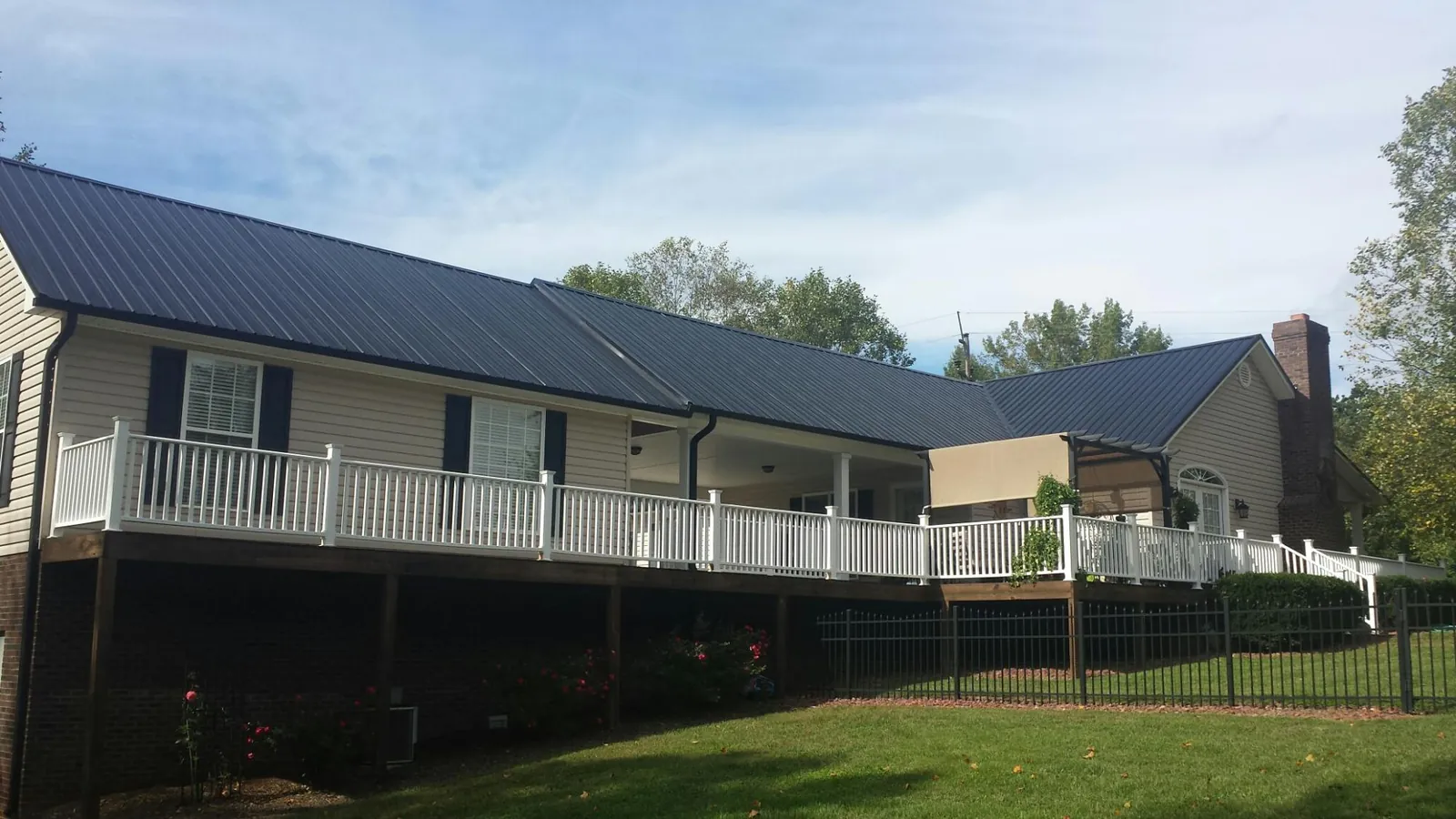 Black metal roof above a long white railed deck on a hillside home in New Orleans