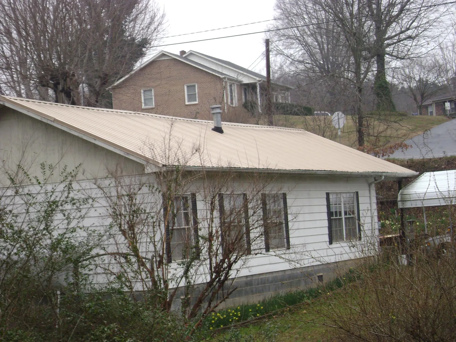 Tan metal roof on a white sided house set into a hillside — Commercial Roofing by Roofing Brothers in New Orleans